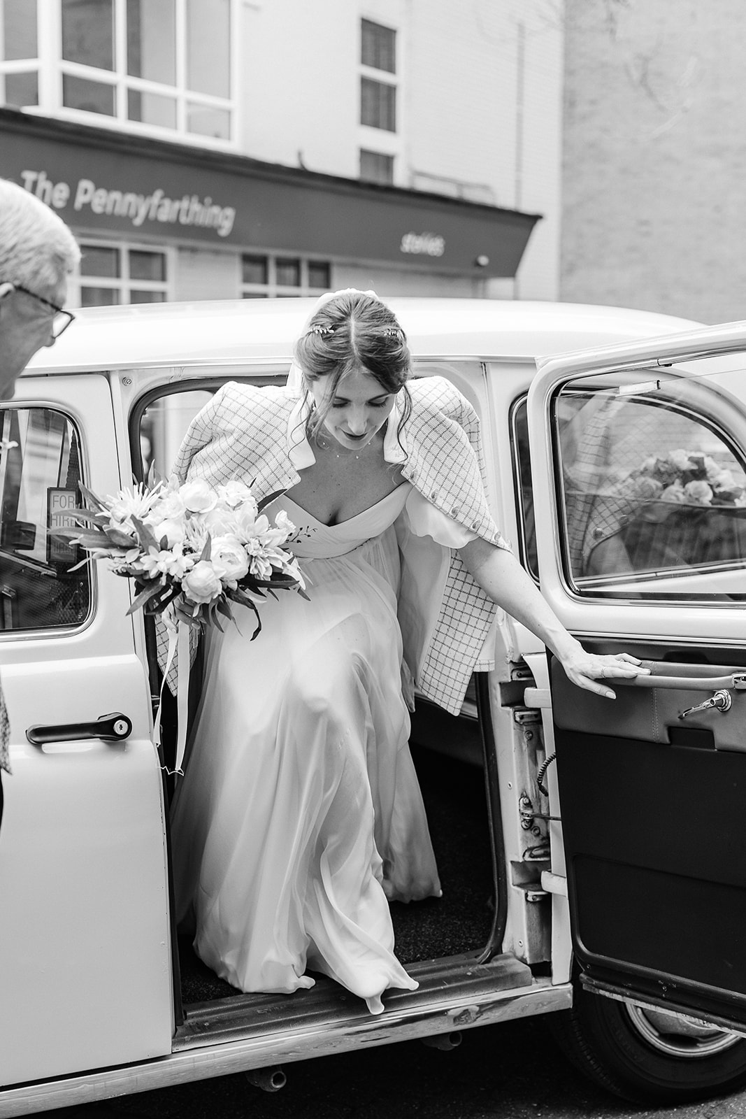 Black and white image of bride stepping out of wedding taxi