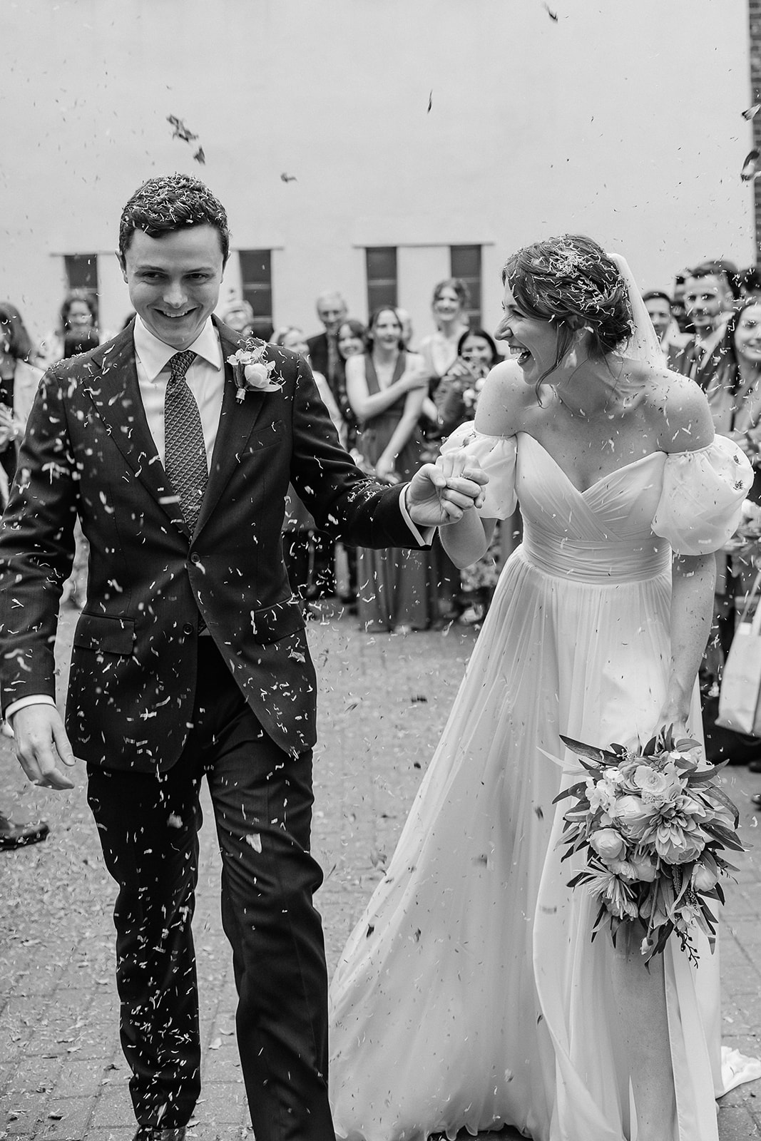 Black and white photo of bride and groom walking through confetti
