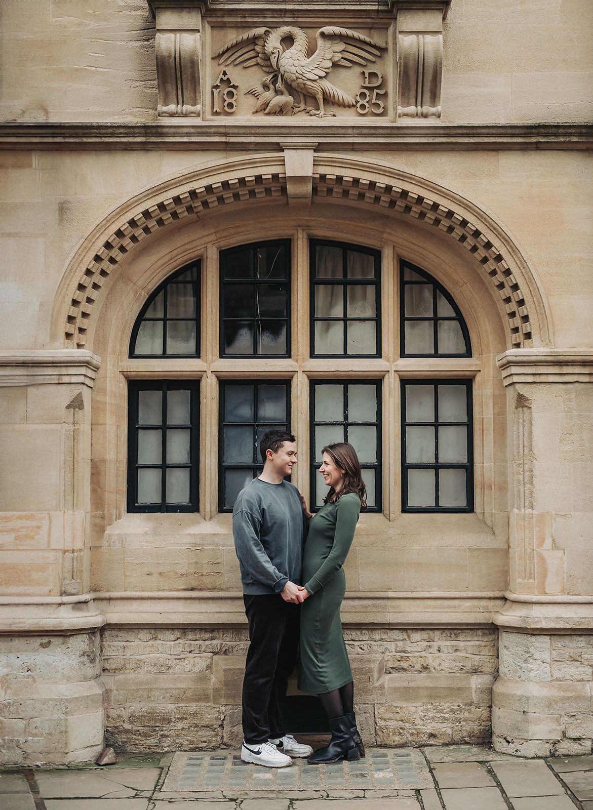 Couple in archway in Oxford smiling at eachother during engagement photoshoot