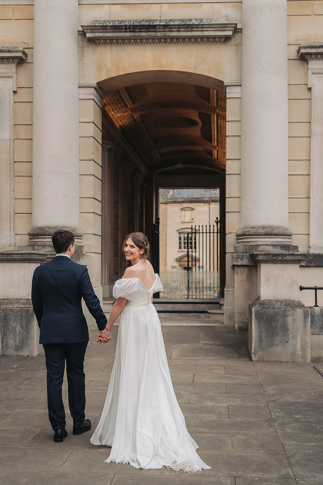 Bride smiling at camera holding hands with groom at Ashmolean Museum