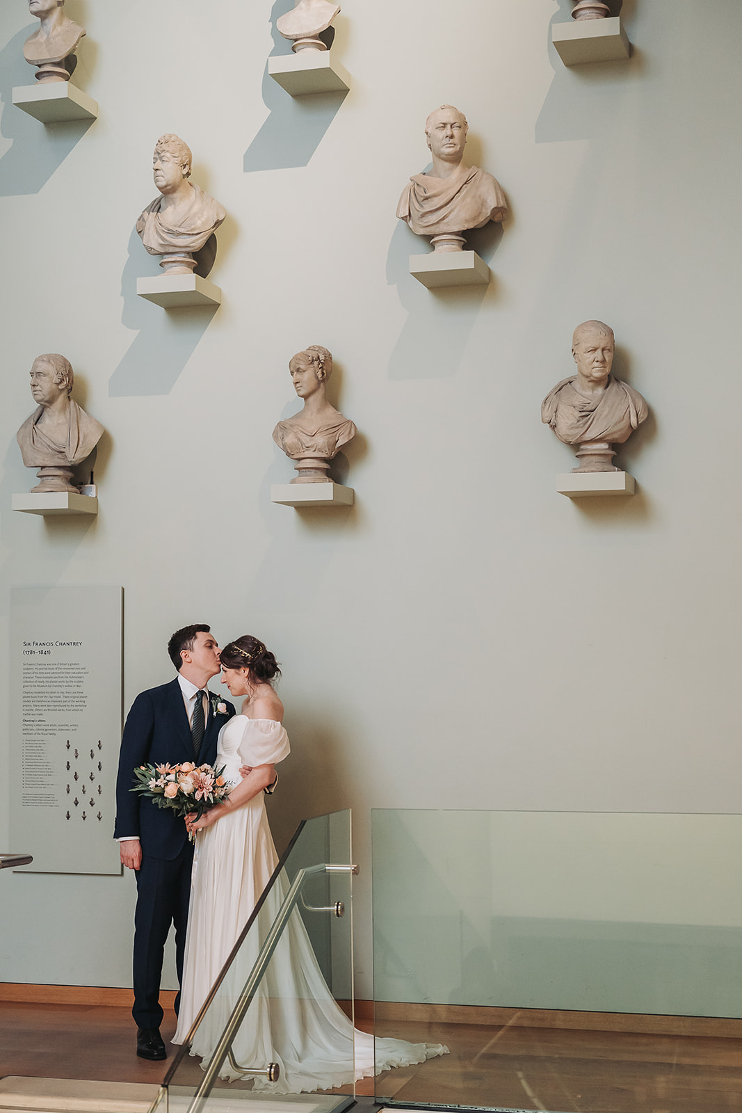 groom kissing bride in front of busts at Ashmolean Museum
