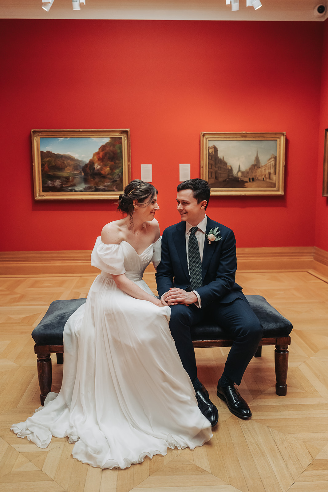 Bride and groom sat looking at eachother in art gallery of Ashmolean Museum
