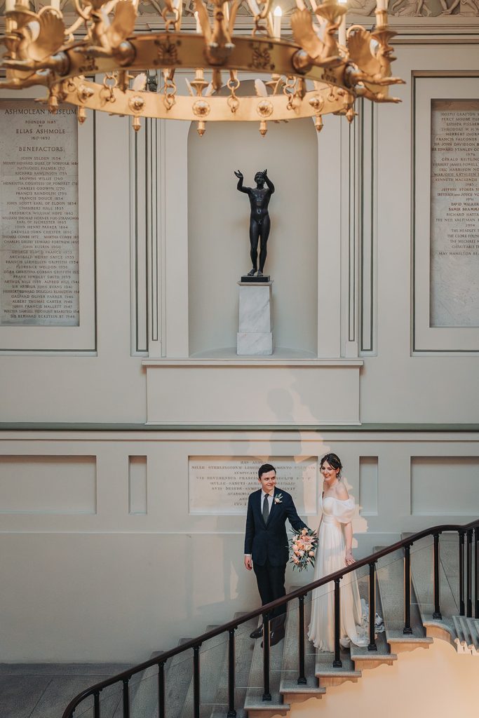 Bride and groom walking down the stairs holding hands at the Ashmolean museum