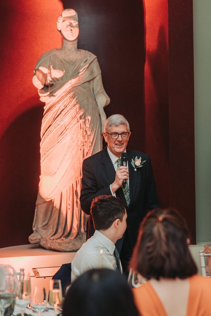 Father giving speech with greek statue behind