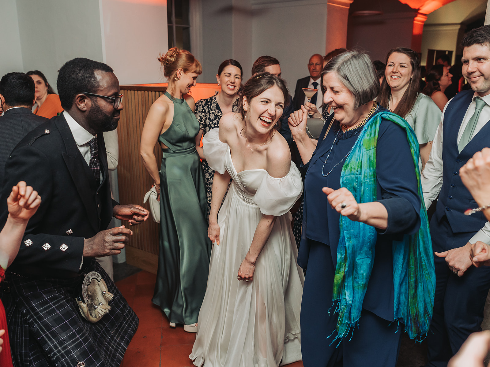 Bride on dancefloor laughing with woman in blue scarf