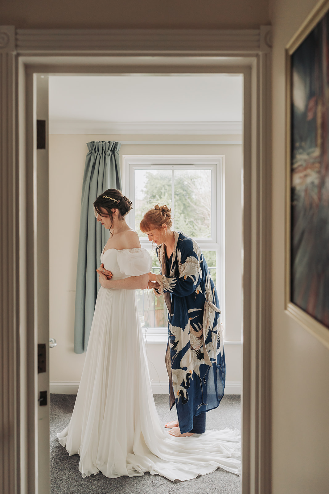 Bridesmaid in floral dressing gown doing brides dress up in doorway at an Oxford wedding