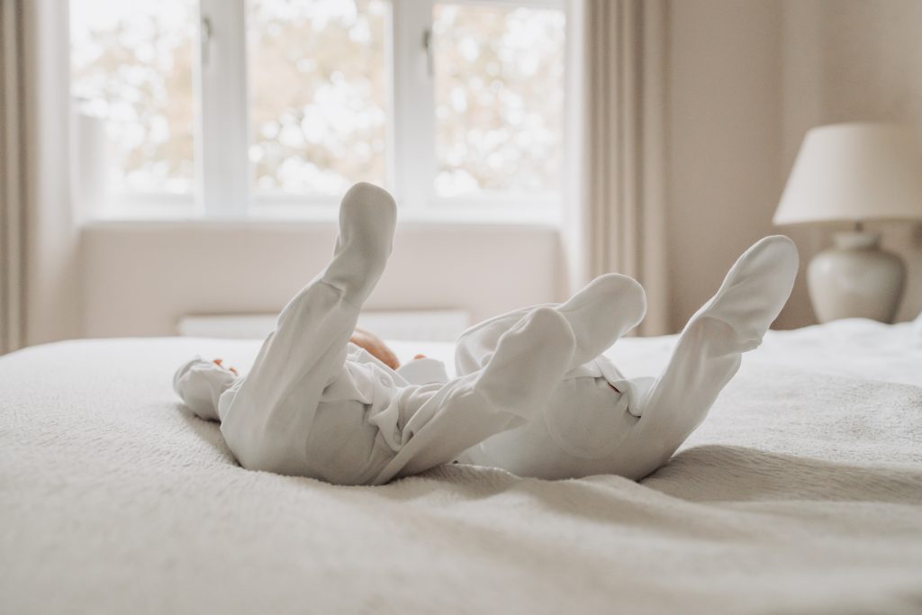 Feet of twin babies lying on bed in white babygrows