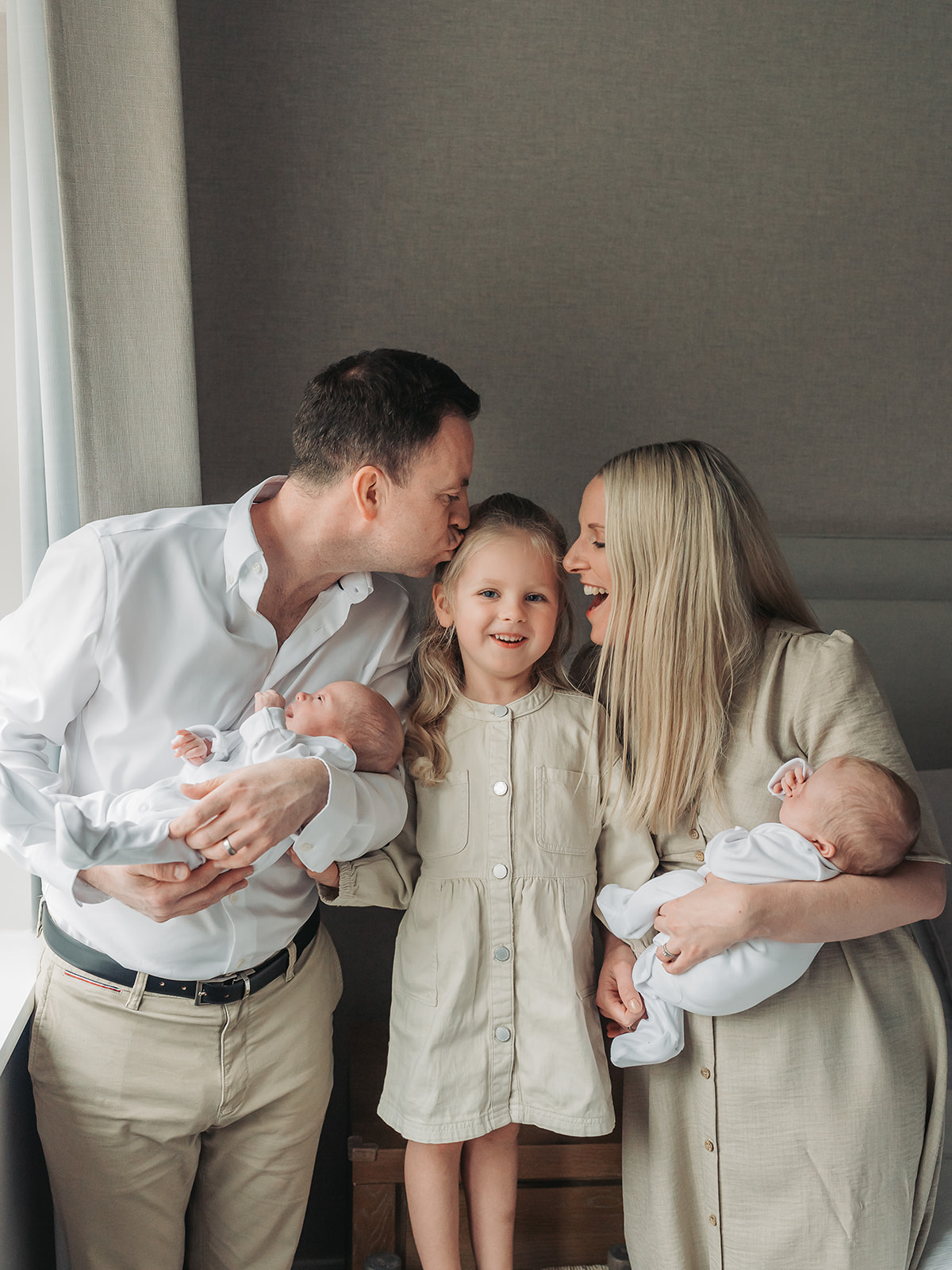 Mum and dad kissing toddler girl whilst holding twins in newborn photoshoot at home