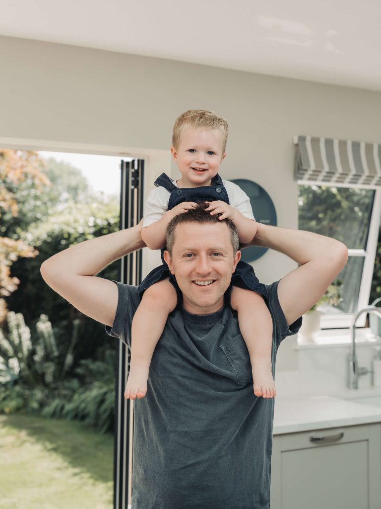 Toddler boy in dungarees on dad's shoulders in kitchen