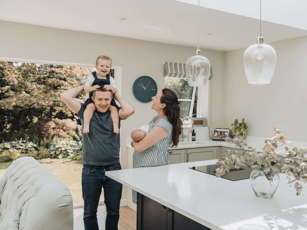 Toddler boy on dad's shoulders and laughing whilst mum and baby look on