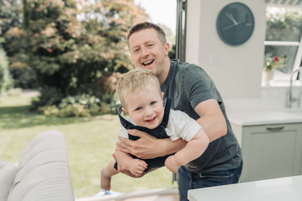 toddler boy smiling at camera whilst being swung like an airplane