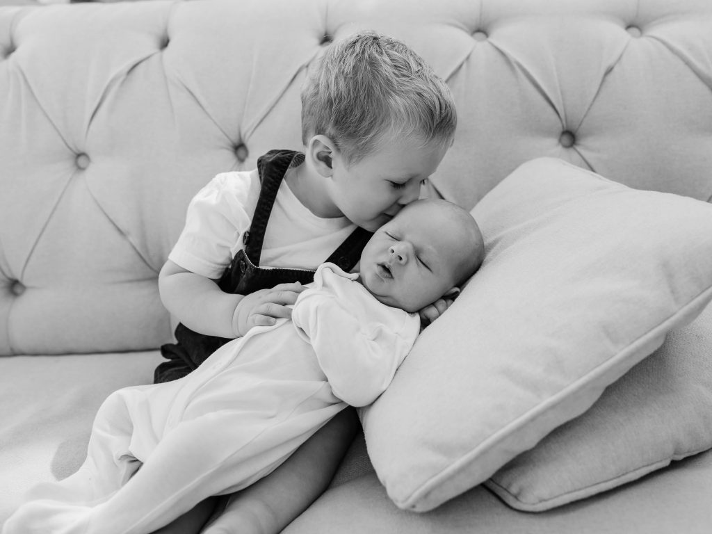 black and white image of toddler boy kissing baby brother