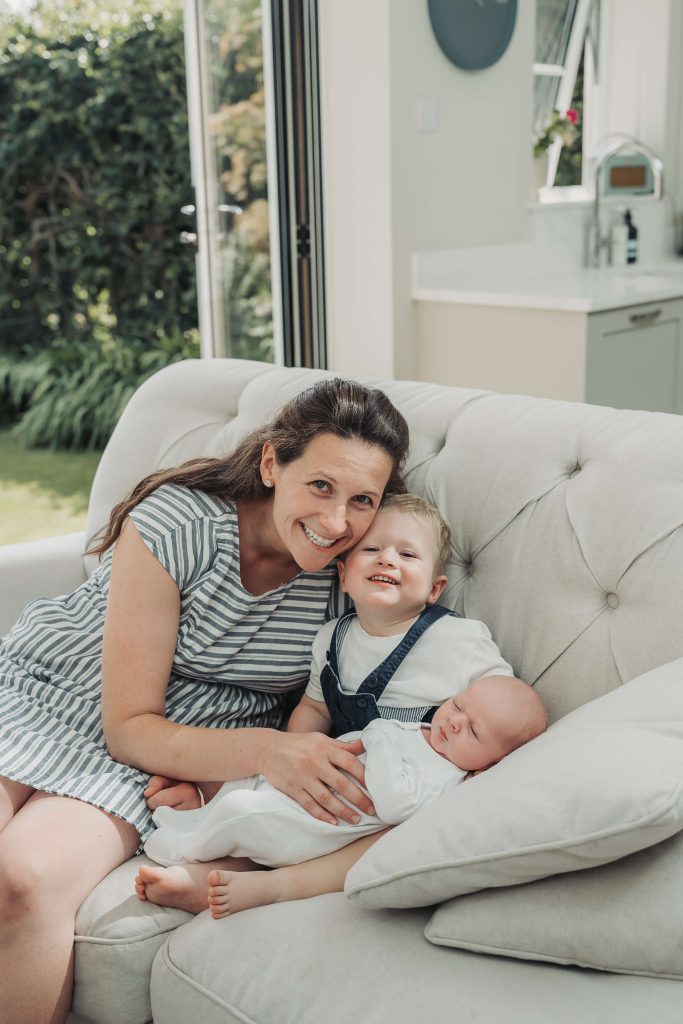 Mum and toddler smiling at camera with newborn baby