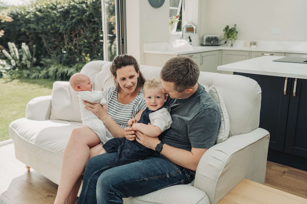 Family sat on sofa in kitchen during a Kenilworth newborn photoshoot