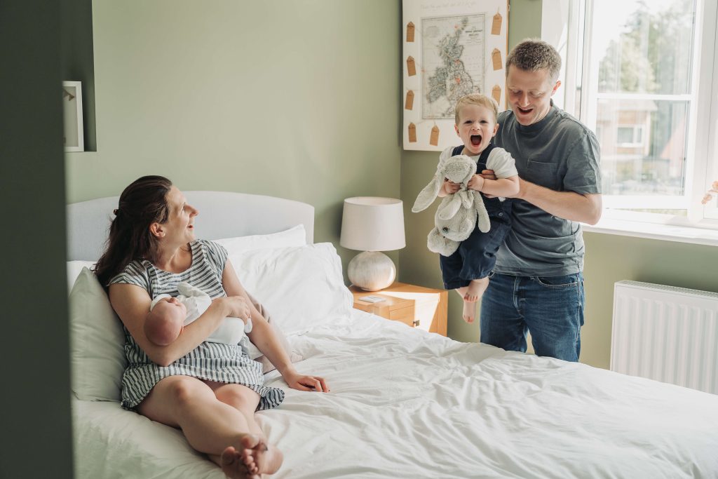 Family in bedroom with dad flying toddler boy in the air