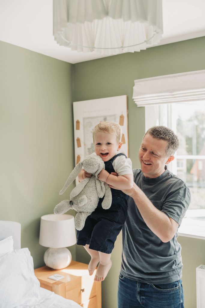 toddler holding large fluffy bunny whilst being lifted in the air by dad