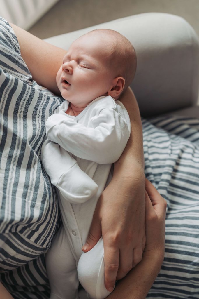 Baby in white babygrow asleep in mum's arms