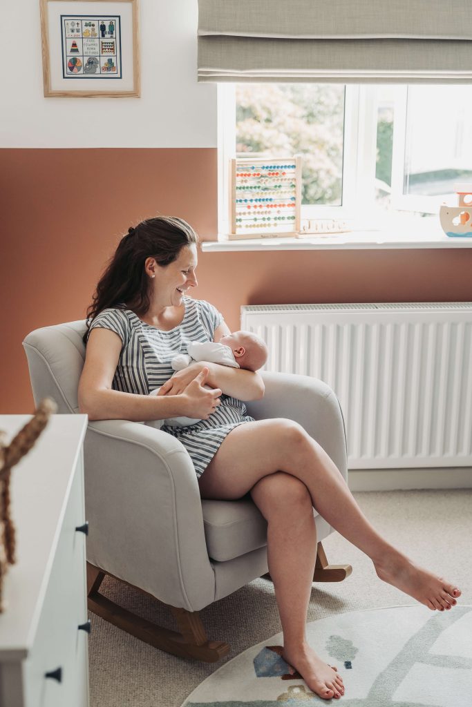 Mum sat in chair in orange nursery holding newborn baby
