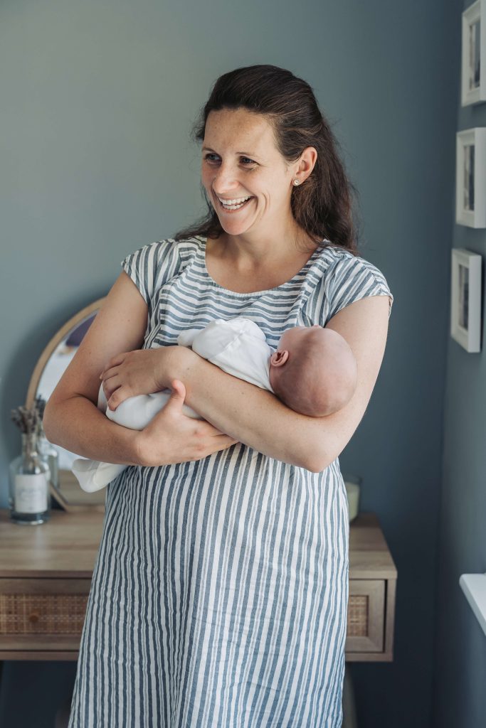 Mum smiling looking away from camera whilst holding newborn baby during photoshoot at home