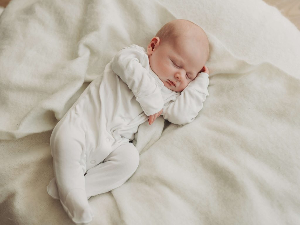 newborn baby lying on white blanket asleep during in home newborn photoshoot