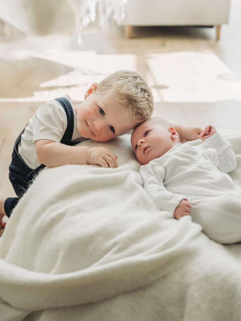 Toddler boy leaning head on baby brother