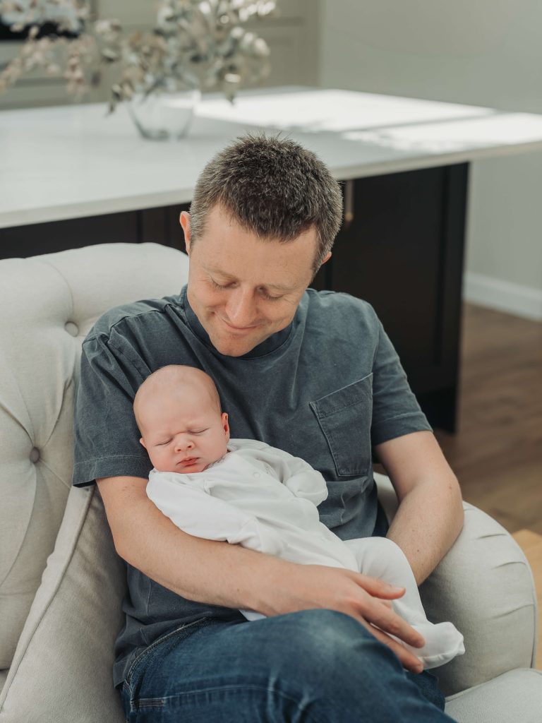 Dad holding sleeping baby whilst looking down and smiling