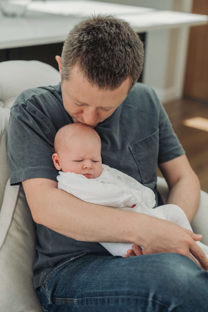 Portrait of dad kissing baby in white babygrow