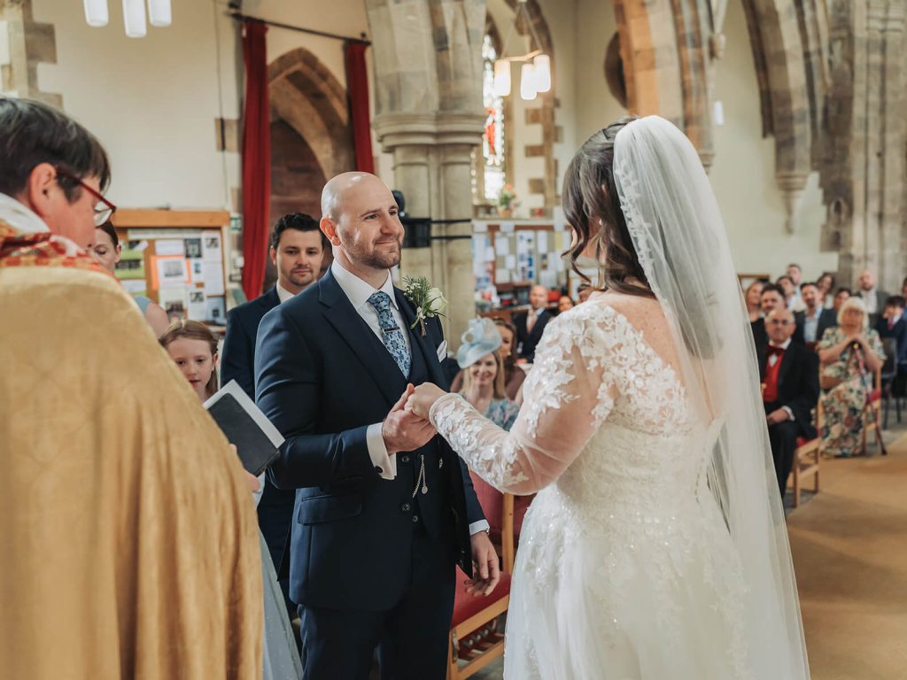 groom smiling at bride in church during vows