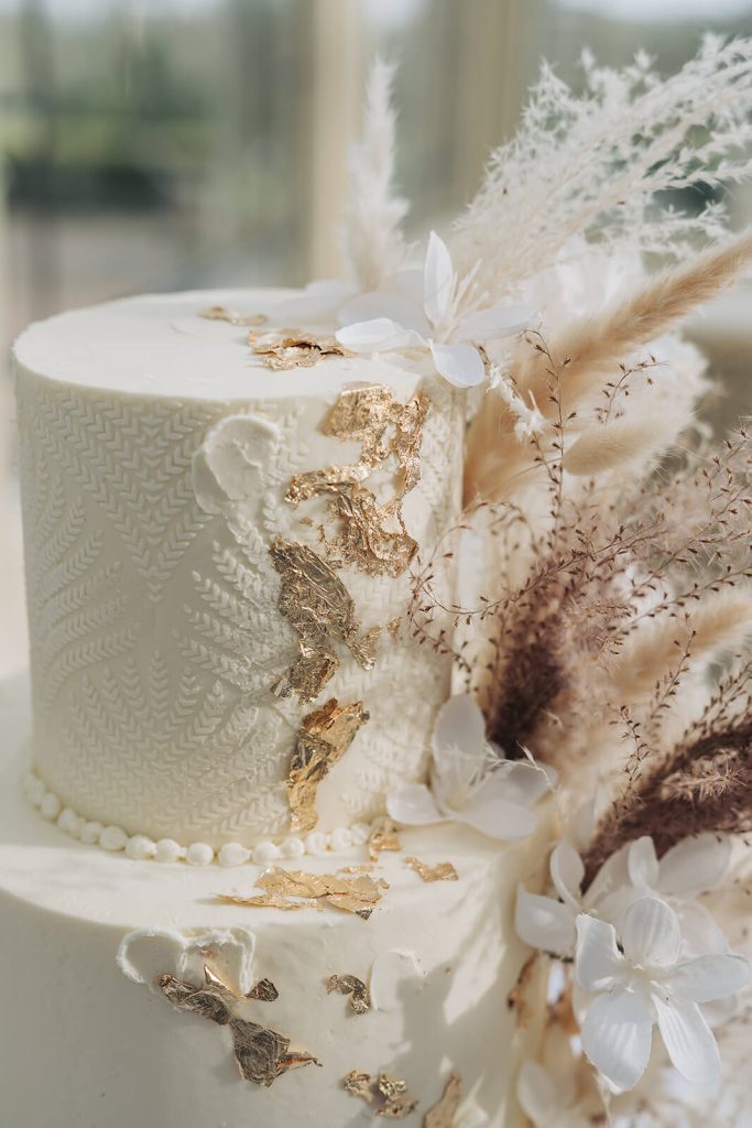 detail shot of gold foil and feathers on white wedding cake