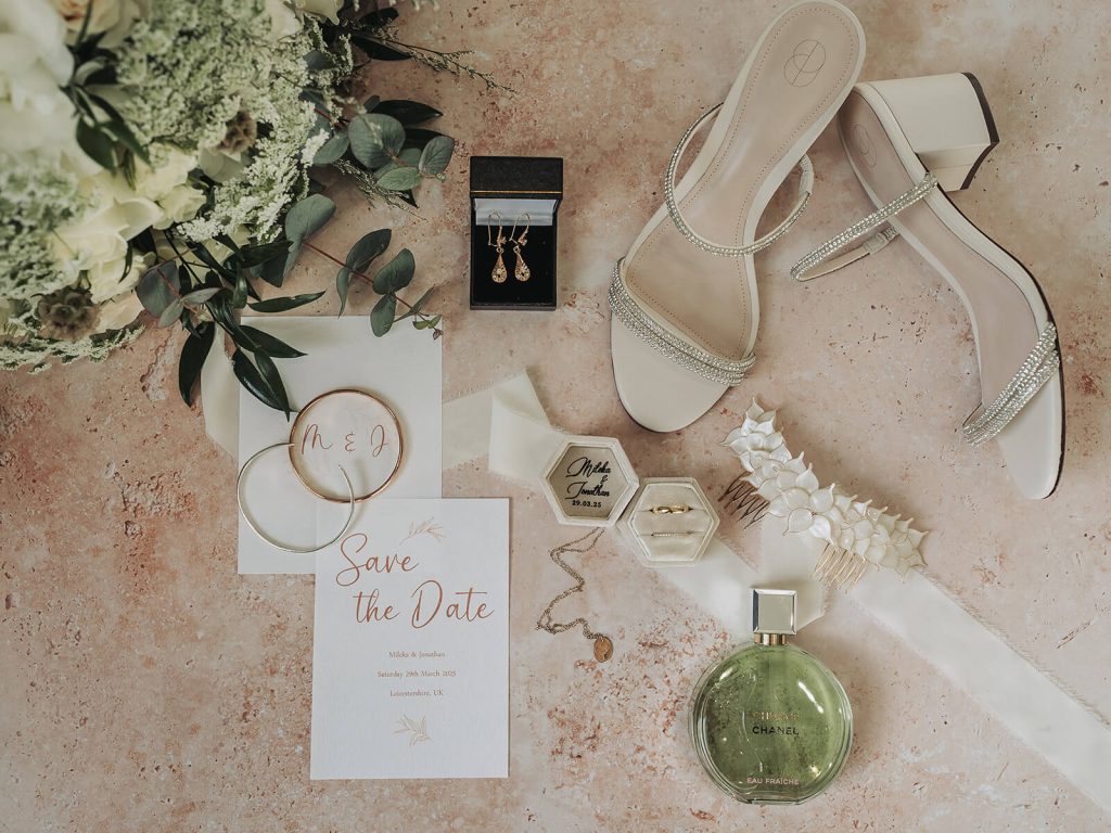 flatlay of wedding details including save the date, shoes and jewellery