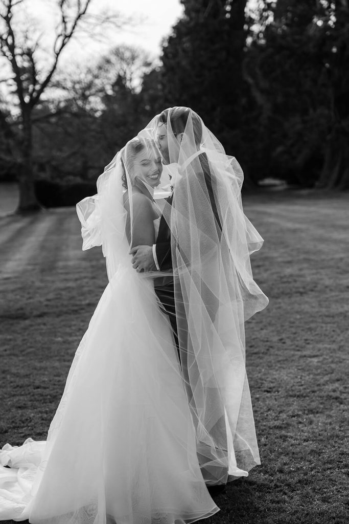 black and white photo of wedding couple under veil