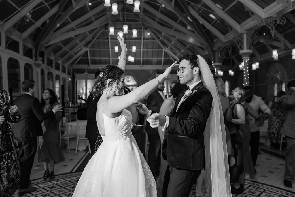 black and white photo of groom wearing veil and dancing with wife