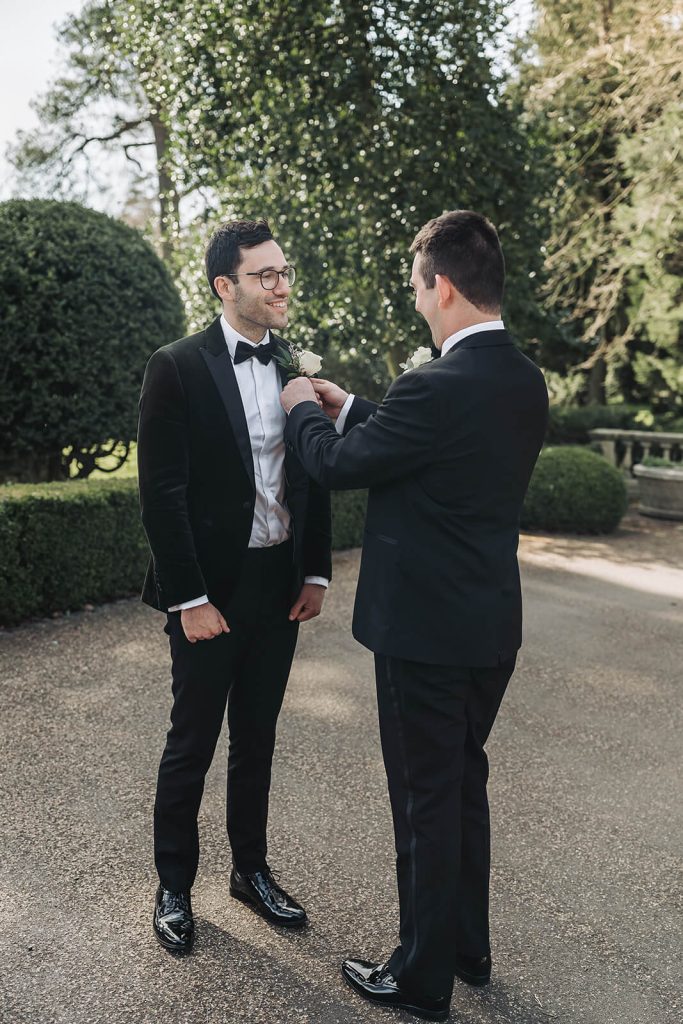 groomsman helping groom in tuxedo get ready