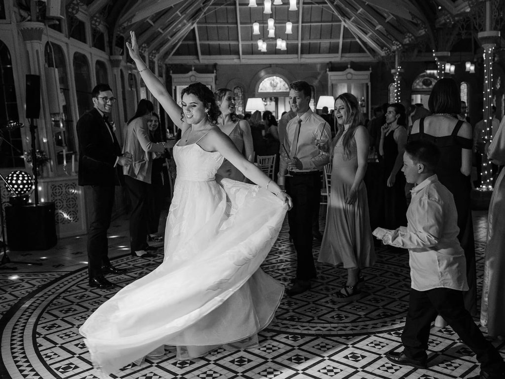 black and white image of bride twirling wedding dress on dancefloor