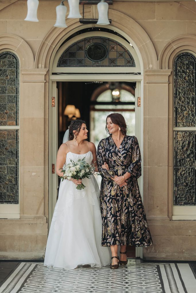 bride and mum walking into Kilworth House wedding ceremony looking at eachother
