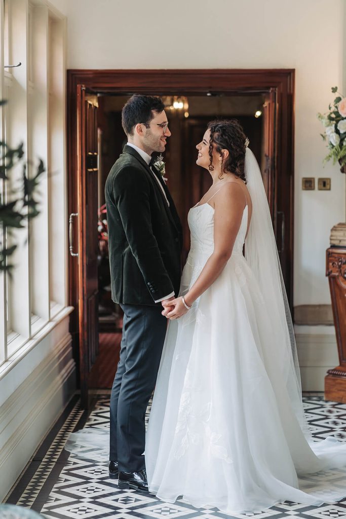 bride and groom holding hands looking at eachother in corridor of Kilworth House