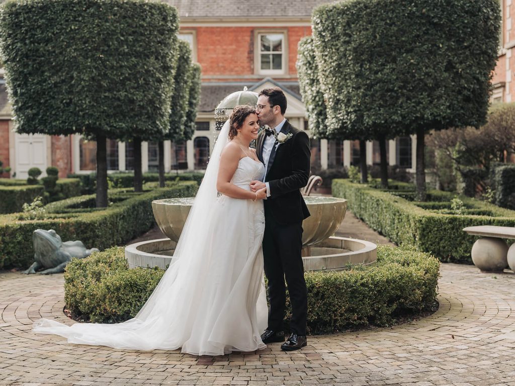 Wedding couple hug and kiss in knot garden at Kilworth House