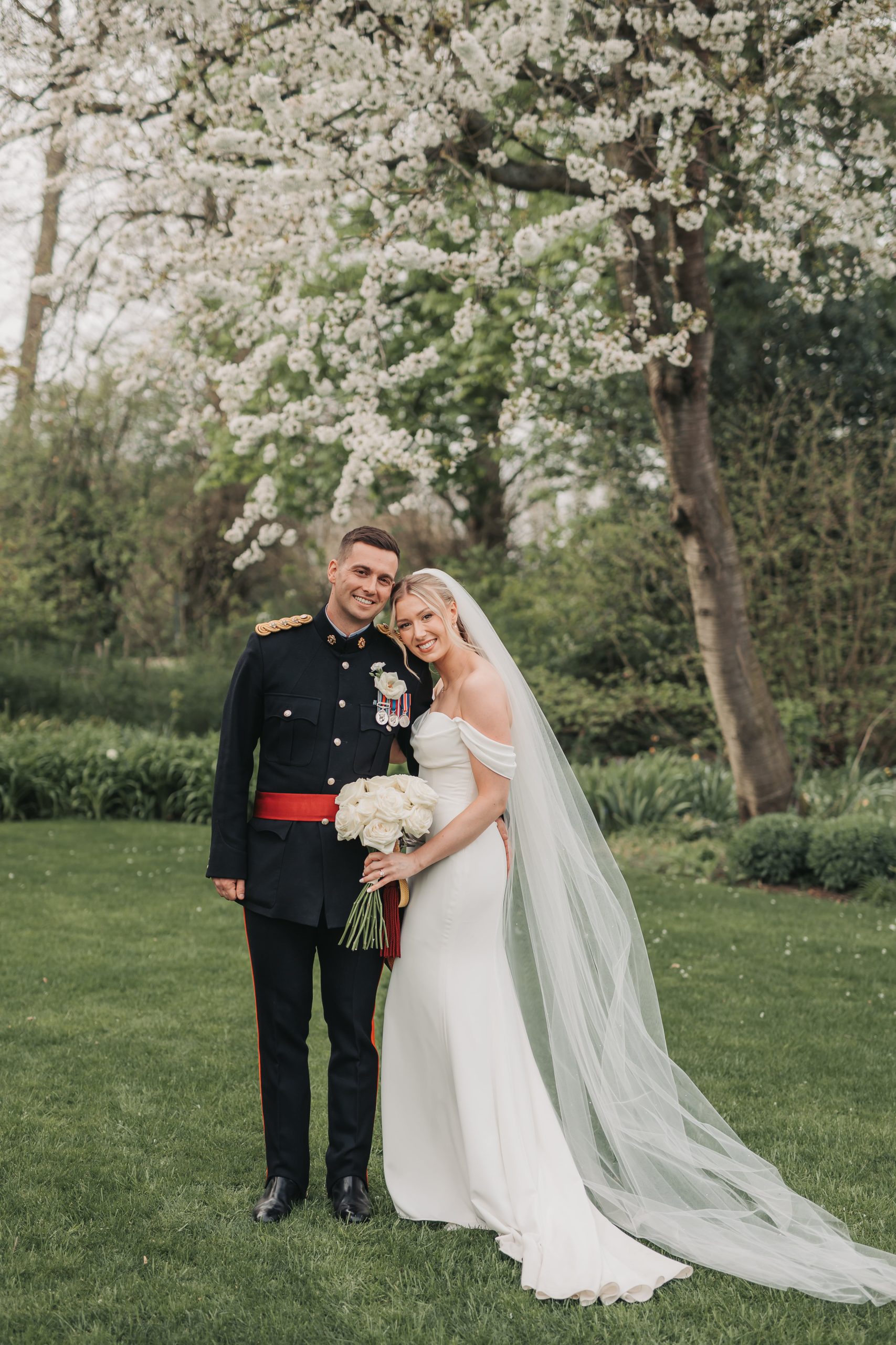 Bride and groom smiling at the camera holding white rose bouquet at Farmhouse at Redcoats wedding venue