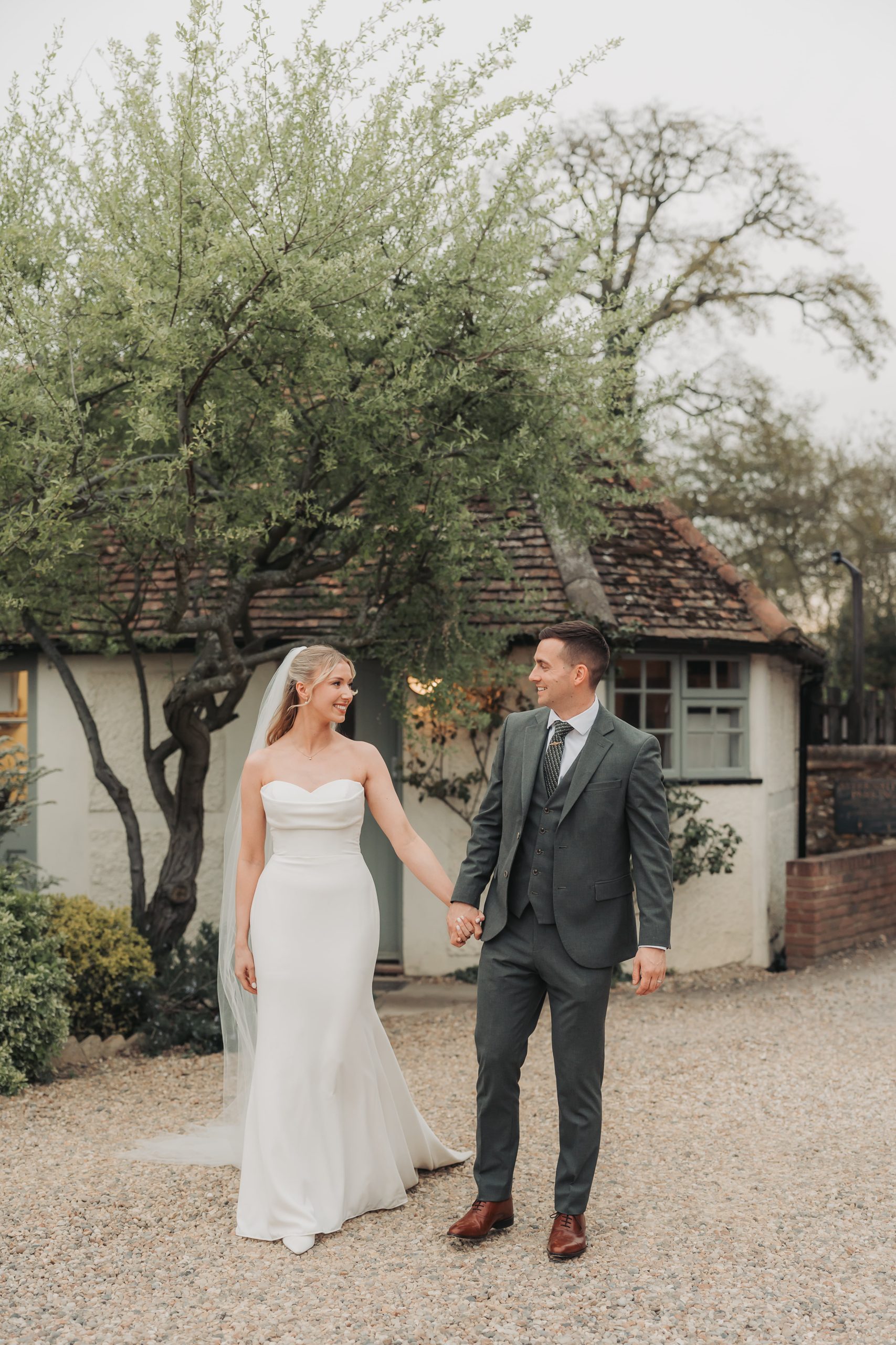 Bride in strapless wedding dress holding hands with groom and walking at Farmhouse at Redcoats