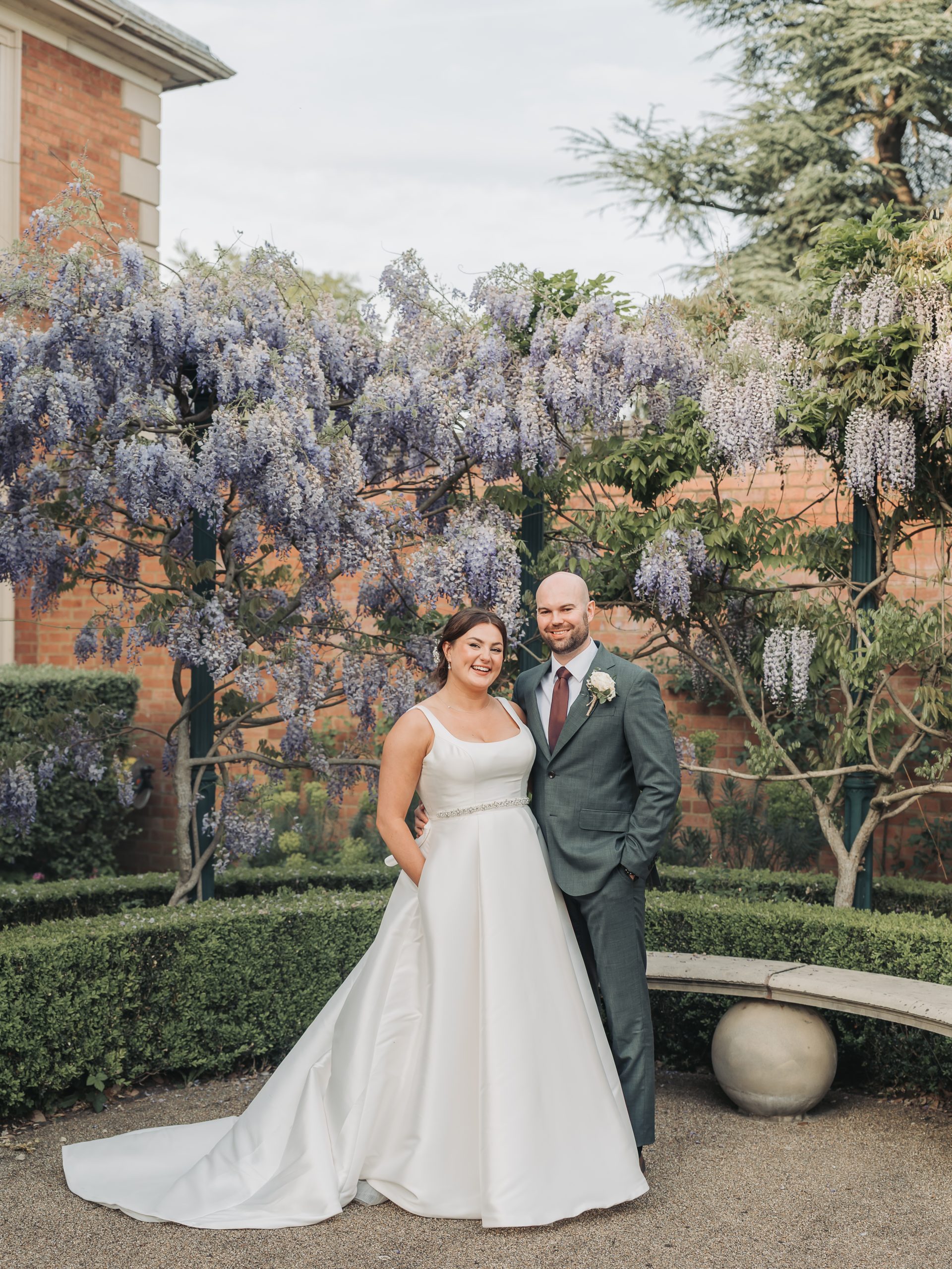 Bride and groom smiling in front of purple wisteria at Kilworth House