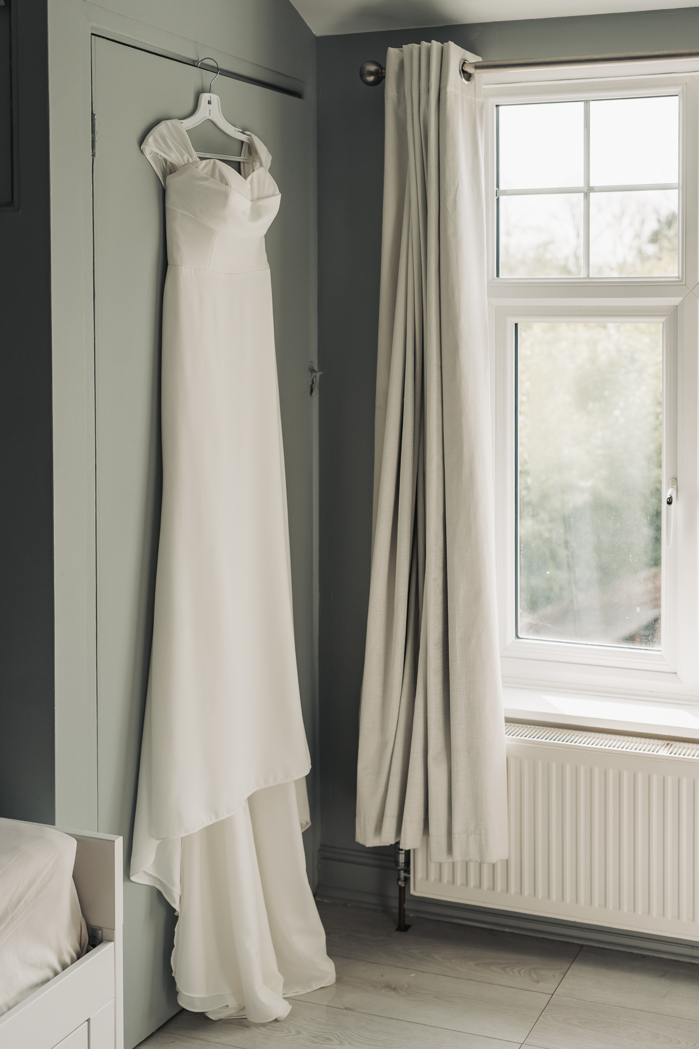Wedding dress hung up against green wall at home in Hitchin