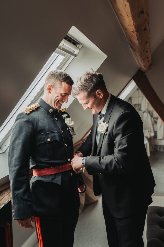 groom in formal military uniform getting dressed with friend